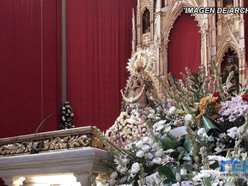 Venerada imagen de la Virgen María adornada con flores y ubicada en un altar ornamental, en un ambiente religioso.