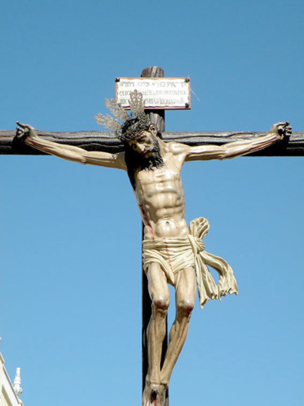 Cruz de Cristo con un crucificado en el centro, sobre un fondo de cielo azul. La cruz tiene una placa con texto en la parte superior.