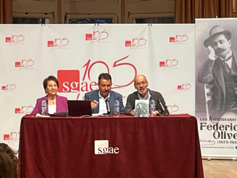 Una conferencia de prensa en un evento de la SGAE (Sociedad General de Autores y Escritores) con tres personas sentadas en una mesa roja frente a un fondo blanco con el logotipo de la SGAE y la frase "130 ANIVERSARIO".