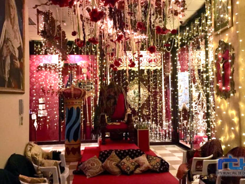 Dormitorio con cama roja, almohadas de colores y decoración navideña con luces y adornos.