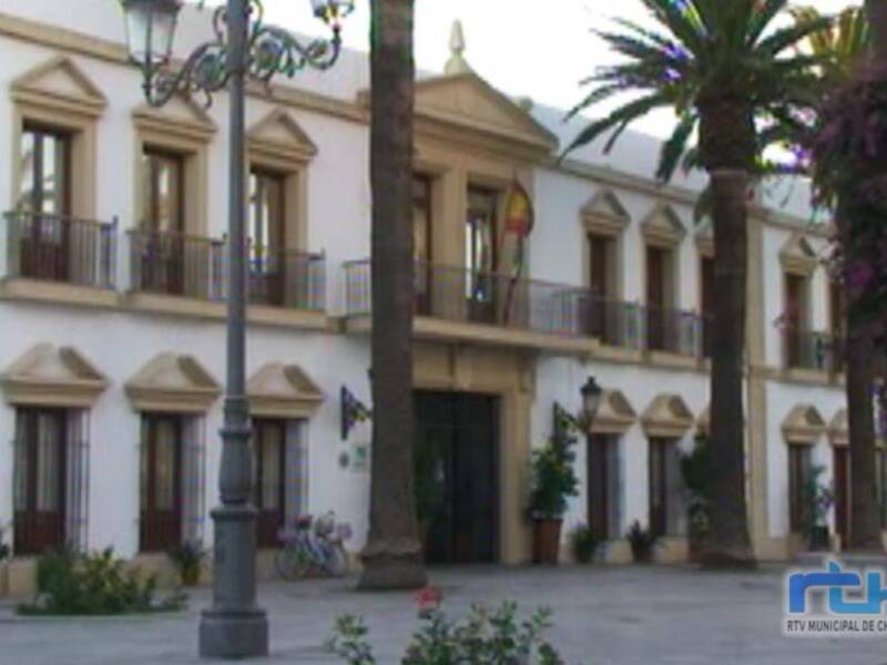 Plaza pública con edificios coloniales, palmeras y flores.