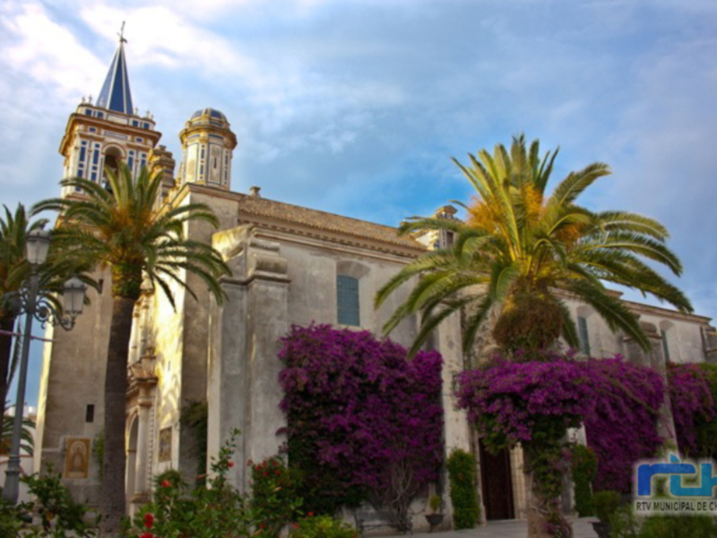 Iglesia con torre y cúpula azul, palmeras y flores en primavera.