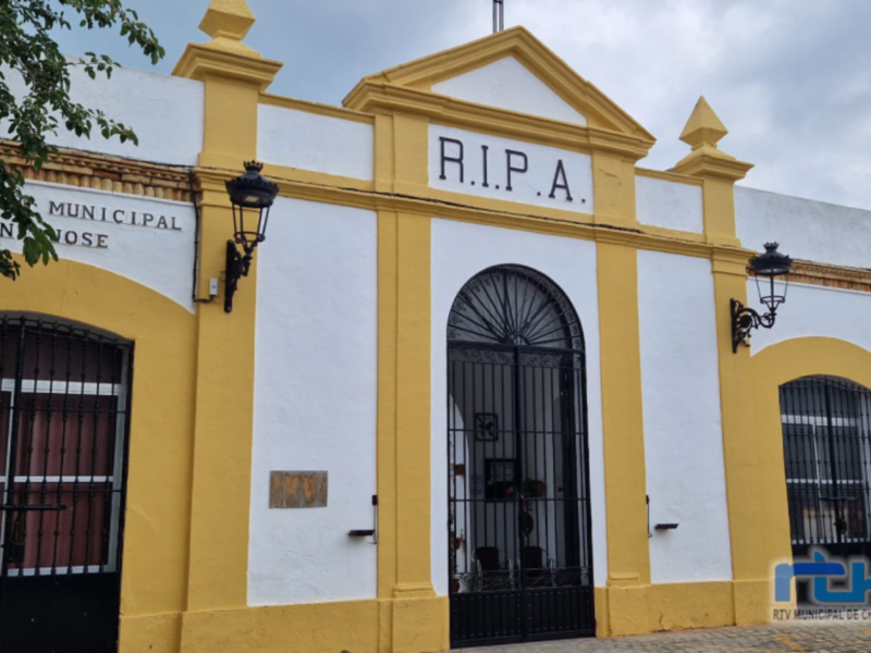 La fachada de un edificio blanco y amarillo con el nombre "R.I.P.A." en letras grandes. La entrada principal está protegida por una puerta de hierro forjado, y hay un letrero adicional con el nombre "MUNICIPAL". La estructura tiene detalles arquitectónicos y una decoración típica de la región.