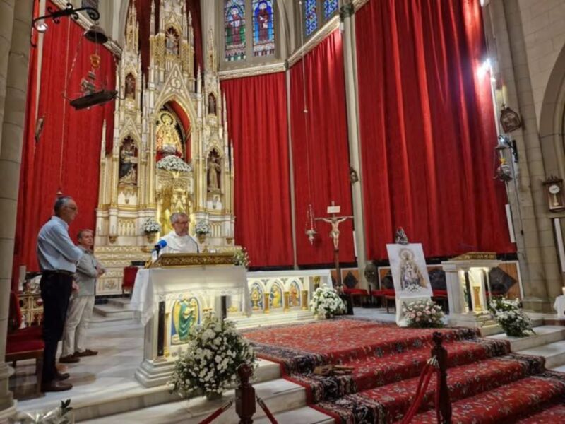 Interior de una iglesia con altares y flores, donde se celebra una misa.