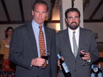 Dos hombres en traje disfrutan de una copa de vino en un ambiente social.