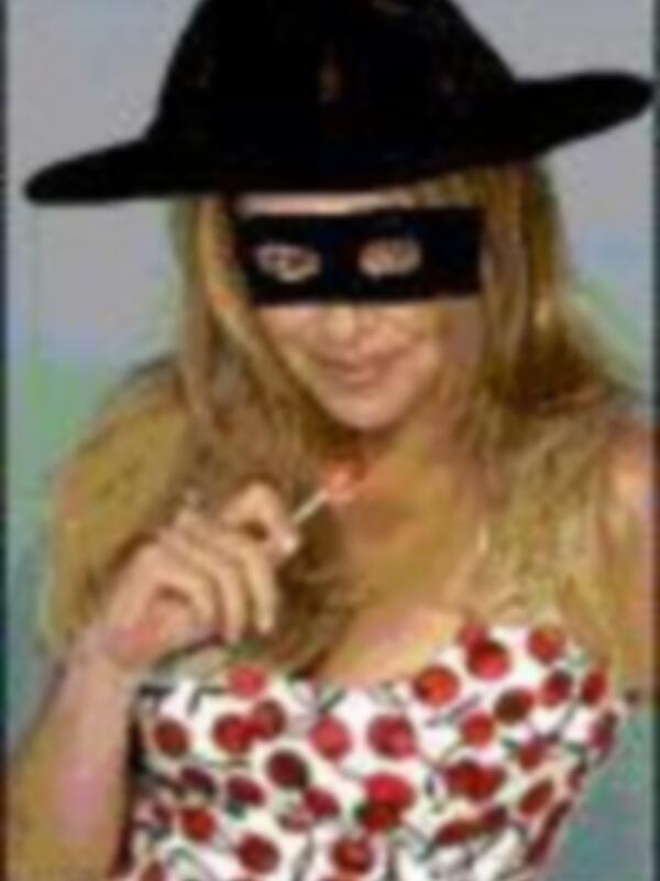 Una mujer con un sombrero negro y una máscara que cubre su rostro, posando con los brazos levantados y una expresión de alegría.