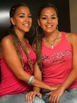 Dos jóvenes sonrientes con trenzas, una con un top rosa y la otra con un top de letras rojas.