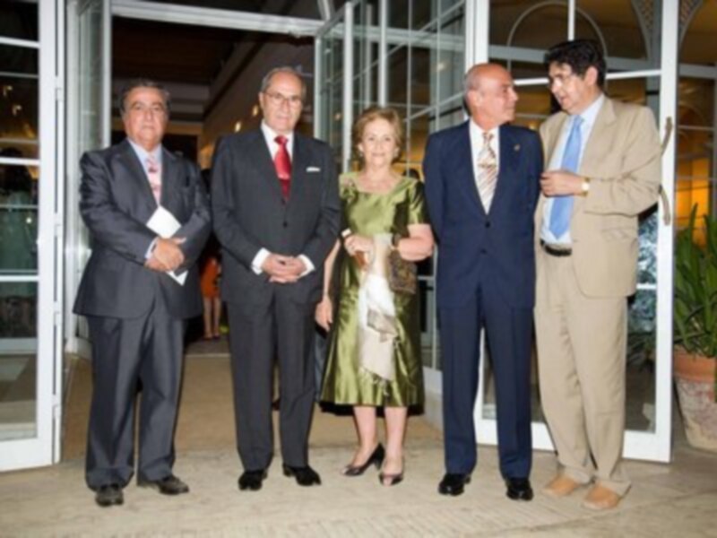 Grupo de personas en trajes formales, posando frente a una estructura metálica con ventanas.