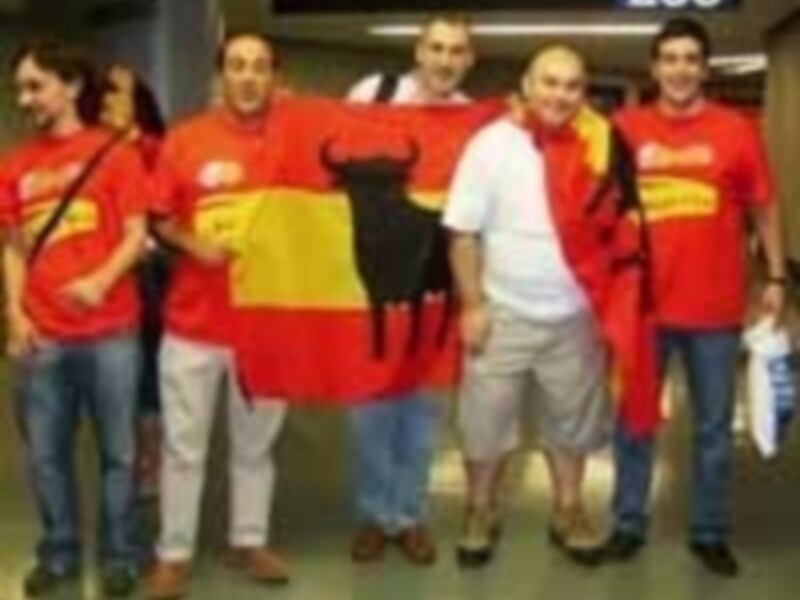 Grupo de personas con camisetas rojas y una bandera española con un toro negro, posando en una estación de metro.