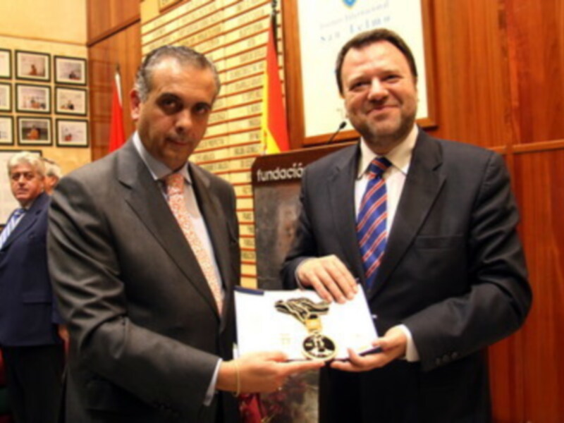 Dos hombres en trajes intercambian un premio o reconocimiento en un entorno formal.