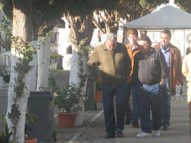Un grupo de personas caminando por un camino en un entorno rural, con árboles y una estructura blanca al fondo.