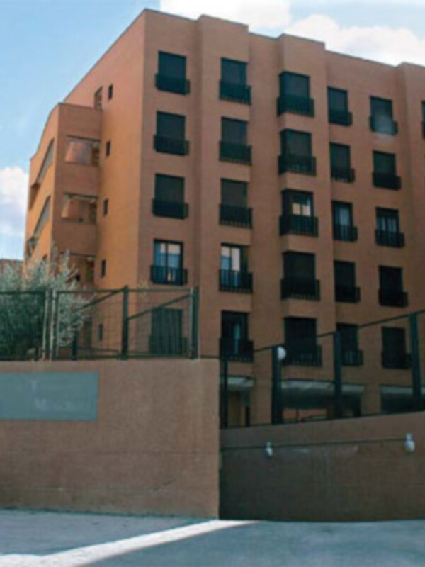 Edificio con balcones y ventanas en una ciudad moderna, con cielo azul y nubes dispersas.