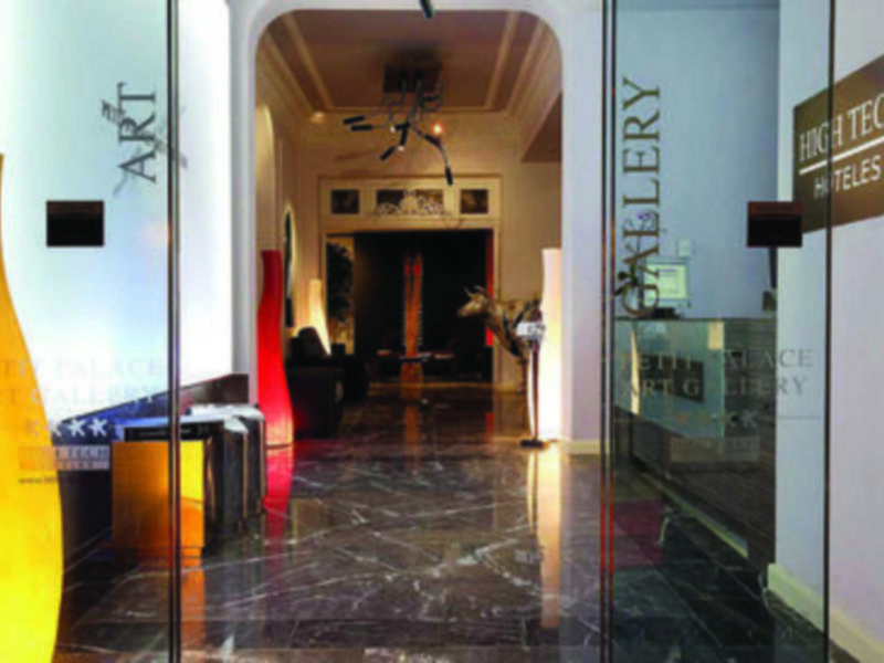 Puerta de cristal con letras "ART" y "TECH". Interior con muebles modernos y una lámpara colgante.