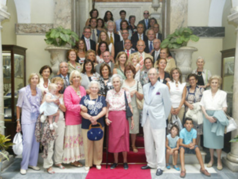 Una familia numerosa y diversificada posando para una foto en un entorno elegante, con columnas y plantas.