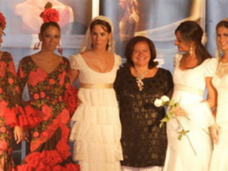 Una mujer en un vestido blanco con velo, rodeada de otras mujeres en trajes tradicionales españoles.