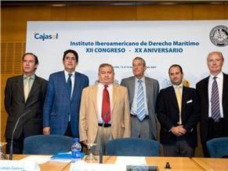 Un grupo de personas en un evento formal, posiblemente un congreso o aniversario del Instituto Iberoamericano de Derecho Marítimo, en una sala con carteles y sillas.