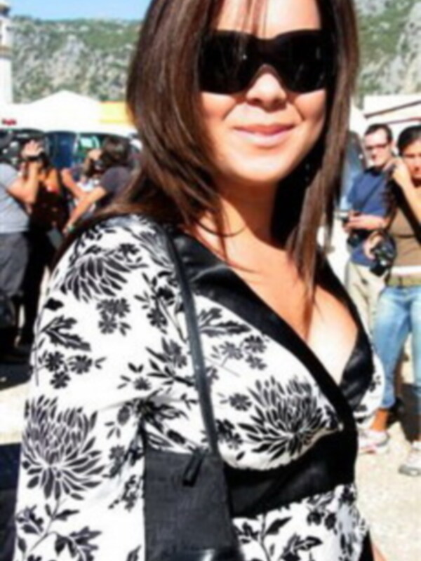 Una mujer con un vestido negro y blanco con flores, posando en un evento al aire libre con montañas en el fondo.