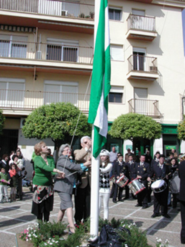 Una celebración en un barrio con una bandera ondeando en el fondo y personas vestidas formalmente.