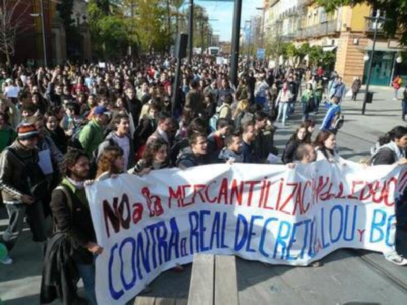 Un grupo de personas marchando por una calle con un cartel que dice "No a la mercantilización de la educación contra el Real Decreto-Ley B".