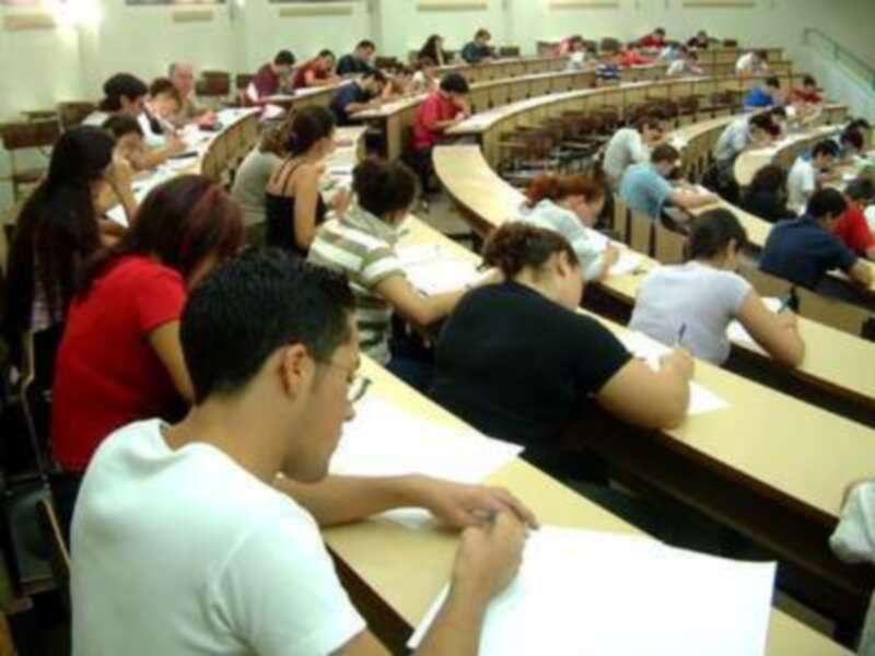 Estudiantes en una clase de universidad, sentados en mesas redondas y trabajando con libros y cuadernos.