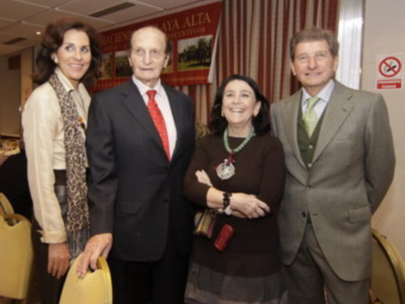 Cuatro personas sonrientes posando juntas en un evento formal, rodeadas de carteles y decoración.