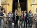 Un grupo de personas vestidas formalmente se encuentran frente a una iglesia, sosteniendo antorchas y símbolos religiosos. La escena sugiere una celebración o ceremonia religiosa en un entorno histórico.