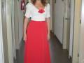 Elegante mujer con vestido rojo y blusa blanca con detalles de lentejuelas, caminando por un pasillo interior.