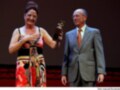 Una mujer en un vestido colorido recibe un premio de manos de un hombre en traje.