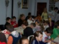 Un grupo de niños y adultos están sentados en una mesa, probablemente en un evento o reunión familiar. La imagen muestra a los niños concentrados en una actividad, mientras algunos adultos observan o participan. La decoración y la iluminación sugieren una atmósfera festiva o familiar.