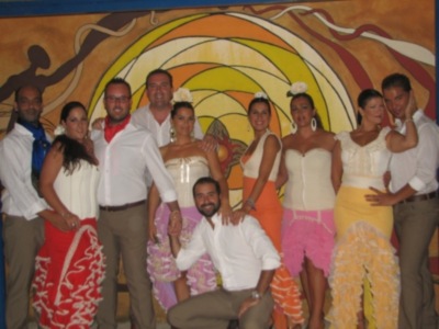 Grupo de personas posando en una fiesta con vestimentas coloridas y un fondo artístico.
