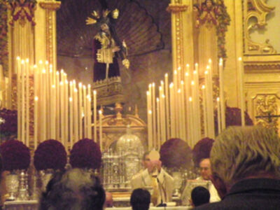 Una procesión religiosa con una imagen de Cristo en la parte superior y una multitud de personas en el primer plano, iluminada por las velas en el altar.