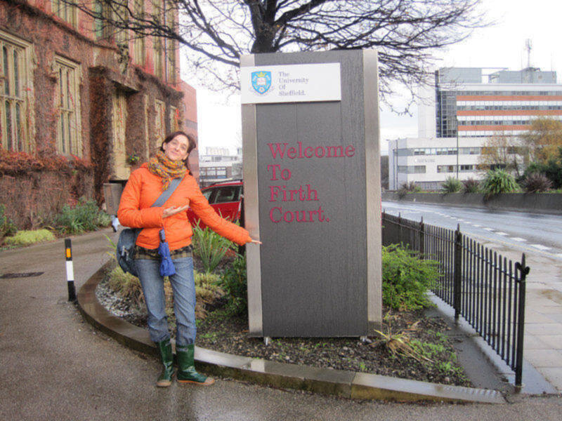 A person standing next to a sign that reads 'Welcome To Firth Court' in front of a building with a red brick facade.