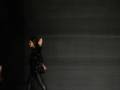 Una modelo camina por la pasarela con un vestido negro brillante, en el fondo se ve una pantalla con las letras "VICKY MARTÍN BERRETO".
