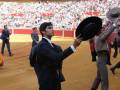 Torero en el ring de la plaza de toros de Sevilla durante una corrida de toros. El torero, vestido con traje y sombrero, se prepara para enfrentarse a los toros. El fondo muestra a los espectadores en la gradas, disfrutando del evento.