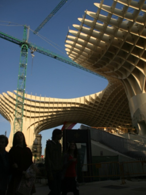 Arco metálico en forma de palmera con personas caminando y una grúa en el cielo.