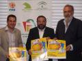 Tres hombres sonríen mientras sostienen folletos de baloncesto. El fondo muestra un cartel con logos de la Federación Española de Baloncesto y la Junta de Andalucía.