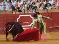 A matador in traditional bullfighting attire performing a pass with a red cape, surrounded by an audience in a bullring.