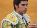 Un torero con traje de cuero dorado y flores, sostiene un vaso mientras mira hacia el lado. Fondo amarillo.