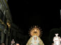 Procesión religiosa nocturna con una imagen venerada en medio de una multitud formalmente vestida.