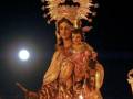 Estatua de la Virgen con el Niño en un evento religioso nocturno, iluminada por una luna llena.