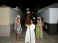 Procesión nocturna con sacerdote y participantes en trajes tradicionales, en una calle urbana.