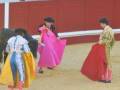 Tres matadores de toros en trajes de luces, uno con capa roja, en una plaza de toros.