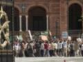 Un grupo de personas protesta frente a un edificio histórico, sosteniendo carteles y pancartas. La imagen muestra una manifestación en un lugar público con una puerta grande y un arco en el fondo.