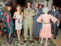 Asistentes a una recepción formal en un salón decorado con elegancia, vestidos y trajes de época.