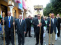 Un grupo de hombres en trajes formando parte de una procesión religiosa, con una estatua en el centro y banderas en el fondo.