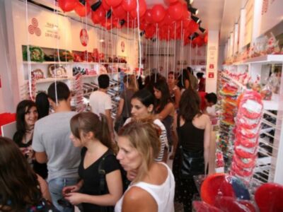 Gente disfrutando en una tienda de dulces con globos rojos colgando del techo.
