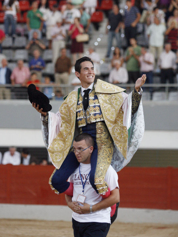 Un torero en traje de capea, sonriendo y saludando a la audiencia en una corrida de toros.