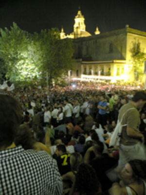 Una multitud en un concierto nocturno frente a una iglesia iluminada.