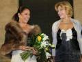 Las dos mujeres sonríen mientras una sostiene un ramo de flores y la otra lleva un abrigo con capucha.