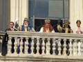 Reyes Magos en trajes tradicionales saludando desde un balcón.
